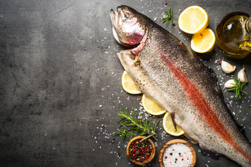 Raw salmon fish whole with ingredients for cookings on black.