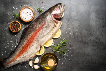 Raw salmon fish whole with ingredients for cookings on black.
