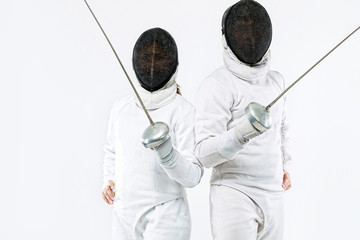 Two Young fencers athletes wearing mask and white fencing costume and holding the sword. Isolated...