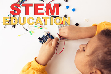 A cute girl constructs robot arduino and program it. The boards and microcontrollers are on the table. STEM education inscription. Programming. Mathematics. The science. Technologie. DIY.  © AlesiaKan