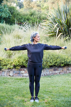 Mature woman with grey hair lifting weights and working out in backyard