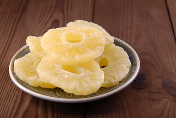 Dry pineapple in sugar on a plate on a brown wooden background.