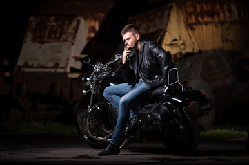 Cute biker in leather jacket sits on a motorcycle. Smoking a cigarette 
