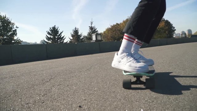 Skateboarder in white sneakers, dark jeans and a plaid shirt rides a skateboard to the camera. Riding on a skateboard outdoors. Slow motion. Hobbies and lifestyle.