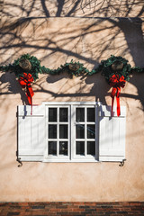 decorative holiday Christmas wreaths hanging above a window on an adobe building