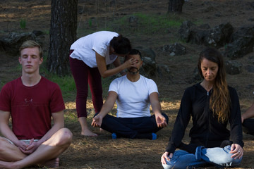 Group of young students following meditation class lead by female teacher in forest park. Woman...