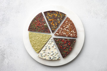 Round chocolate pizza pieces with diverse kinds of chocolate on stone tray on textured background, top view