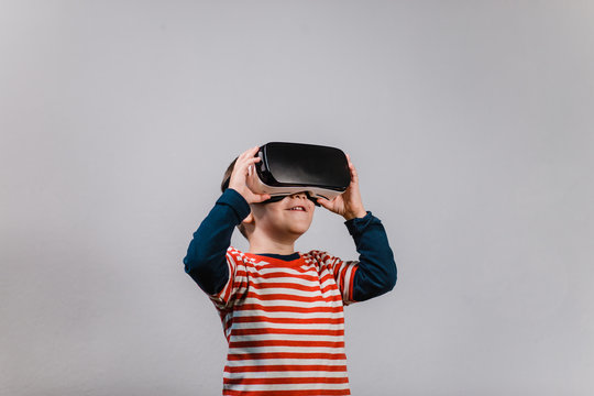Excited kid having fun with VR glasses. Portrait of cheerful child wearing virtual reality headset against grey background.