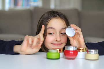 Cute funny sly preteen girl trying mother cosmetics  going to put her finger into cream. Choosing...