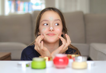 Obraz na płótnie Canvas Cute preteen girl applying various cosmetic creams on face skin secretly. Trying first skin care balm. Assortment of treatment for different skin type. Using mother cosmetics