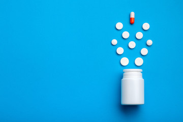 Capsule over the tablets directed in the direction of the bottle for drugs on a blue background top view.