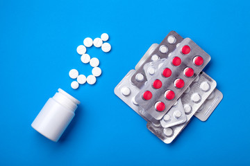 conceptual background on a medical theme pharmaceuticals on a blue background with blisters with pills and a plastic medicine bottle near which is depicted a dollar symbol from round white pills.
