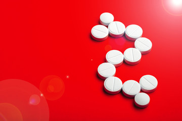 Conceptual background on the commercial theme of pharmacology and the production of medicines and drugs, tablets laid out in the form of a dollar sign on a red background with a sun flare.