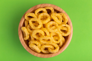 Puff corn rings in wooden bowl on bright colored background