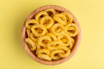 Puff corn rings in wooden bowl on bright colored background