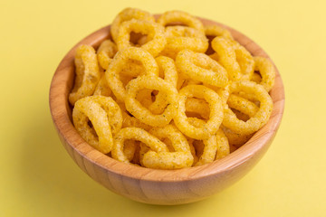 Puff corn rings in wooden bowl on bright colored background