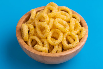 Puff corn rings in wooden bowl on bright colored background