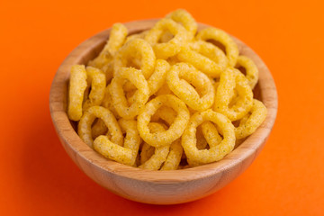 Puff corn rings in wooden bowl on bright colored background