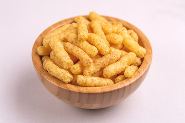 Crispy corn sticks in wooden bowl on light background