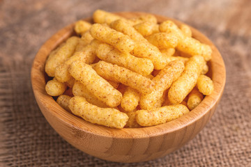 Crispy corn sticks in wooden bowl on burlap napkin
