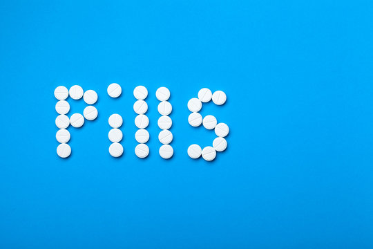 Conceptual background on the medical theme word pills laid out from round white pills on a blue background with copy space for text.
