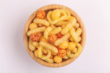 Assorted puff corn snacks in wooden bowl on light background