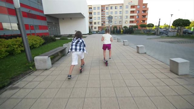 Children Learn To Ride Scooter On Sunny Summer Day. Kids Play Outdoors With Scooters. Active Leisure and Outdoor Sport For Child.