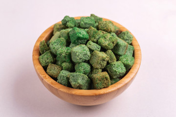 Wasabi flavored crackers in wooden bowl on light marble background