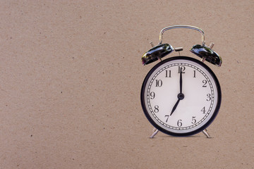Black retro alarm clock at 07:00 o'clock   on brown old paper with space for text