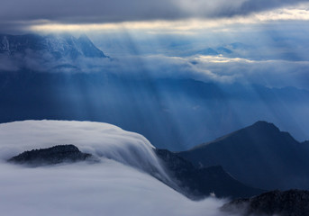 Brilliant rays of sunshine illuminating mountains and valleys below the clouds. Sea of clouds, Mist, Haze, Cloud Waterfall, moody atmosphere, heaven concept, abstract landscape