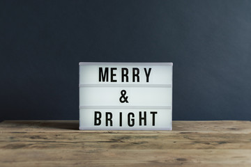 Lightbox with the message Merry & Bright on a wooden surface.