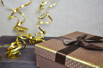 brown and gold box with a gift for Christmas with gold ribbon and bow for a birthday or holiday on a brown wooden background