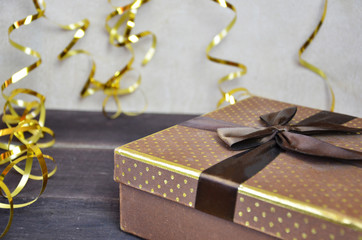 brown and gold box with a gift for Christmas with gold ribbon and bow for a birthday or holiday on a brown wooden background