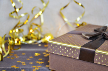 brown and gold box with a gift for Christmas with gold ribbon and bow for a birthday or holiday on a brown wooden background