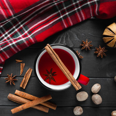 Christmas mulled wine with spices in red mug on wooden background.