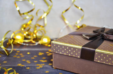 brown and gold box with a gift for Christmas with gold ribbon and bow for a birthday or holiday on a brown wooden background