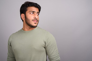 Portrait of young handsome Indian man thinking against gray background