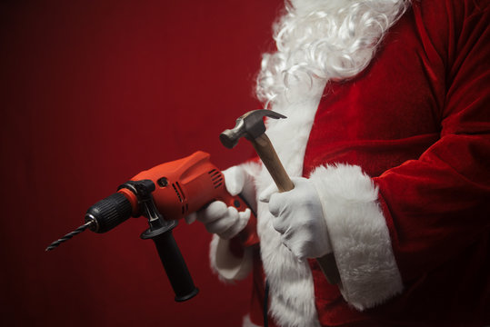 Father Santa Claus holding using electric drill and hammer tools ready to renovate space background. Handyman repairman, festive mood for seasonal business work. Merry Christmas and Happy New Year