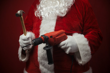 Father Santa Claus holding using electric drill and hammer tools ready to renovate space background. Handyman repairman, festive mood for seasonal business work. Merry Christmas and Happy New Year