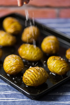 Woman sprinkling sea salt over baked Hasselback potatoes