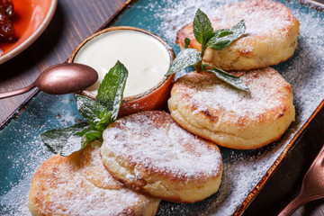 Frying homemade cottage cheese pancakes syrniki with powdered sugar, sour cream, berries jam on plate close up. Traditional Russian cuisine at the Pancake week or Shrovetide. Flat lay. Top view