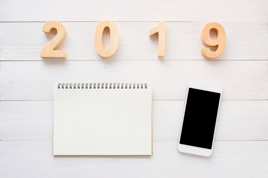 2019 wood letters, blank notebook paper, white smart phone with blank screen on white marble table background, 2019 new year mock up, template with copy space for text, top view