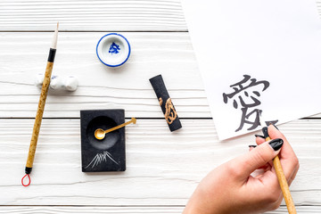 Calligraphy. Hand writes hieroglyph love on white paper on wooden background top view