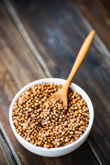 Dried coriander seeds in a bowl with wooden spoon on wooden table, herbs and spices, food ingredients