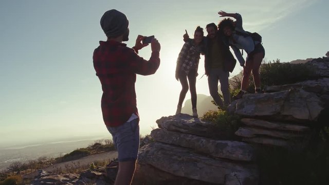 Young man taking picture of his friends standing on rocks during a hike. Group of hikers taking photographs with mobile phone.
