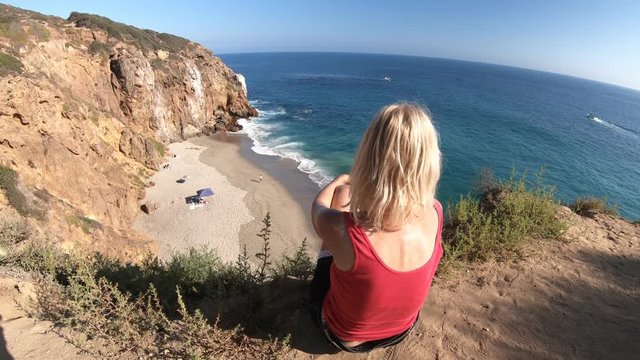 Caucasian female looks Pirates Cove promontory Beach from Point Dume promontory on Malibu coast in CA, United States. Carefree woman enjoys California West Coast. Blue sky, sunny.