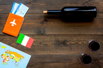 Gastronomical tourism. Italian food symbols. Passport and tickets near italian flag, bottle of red wine, map of the world on dark wooden background top view copy space frame