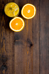 Glass of cold orange juice near halfs of fresh oranges on dark wooden background top view copy space