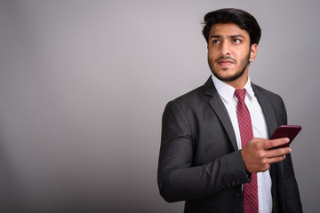 Portrait of Indian businessman using mobile phone against gray background