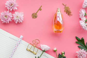 Perfume on feminine desk. Women's accessories. Perfume near notebook for dairy among flowers on pink background top view